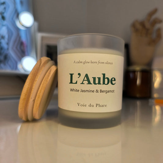 Candle with 'L'Aube' label on a reflective surface