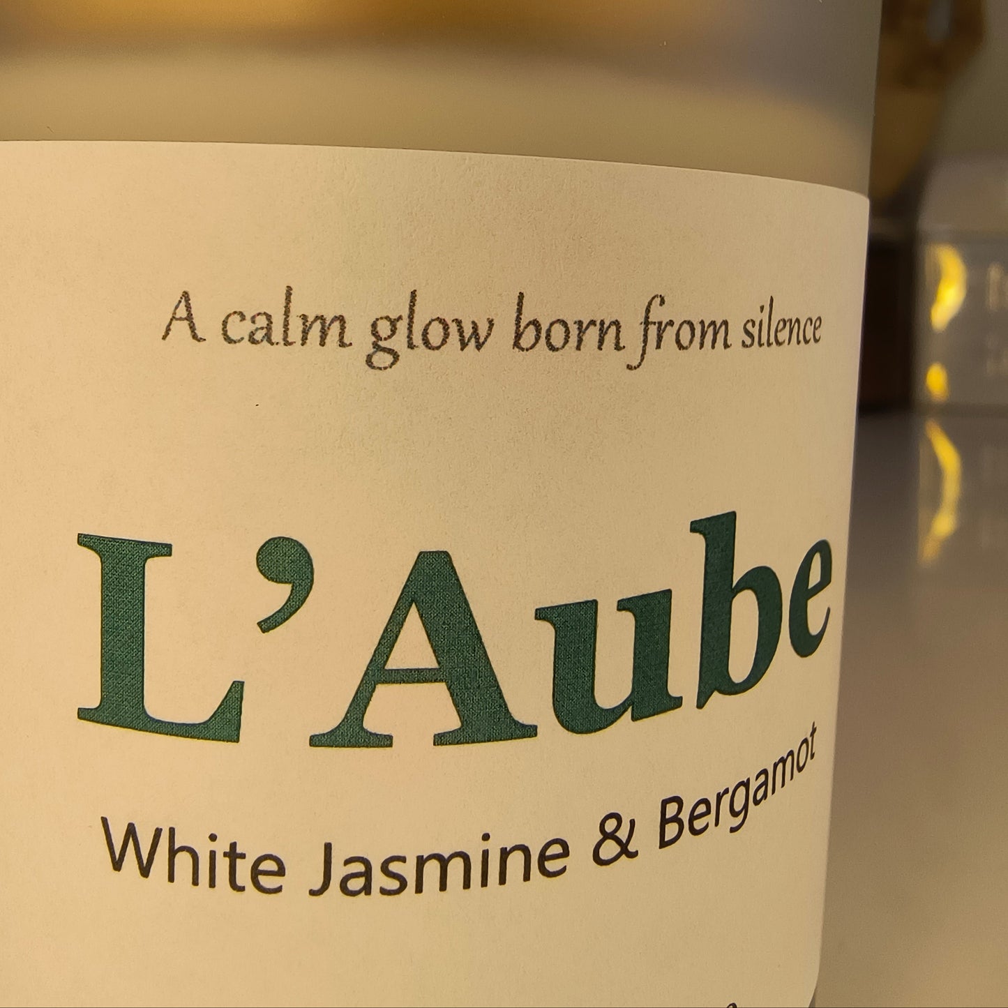 Close-up of a L'Aube candle with 'White Jasmine & Bergamot' text on a beige background