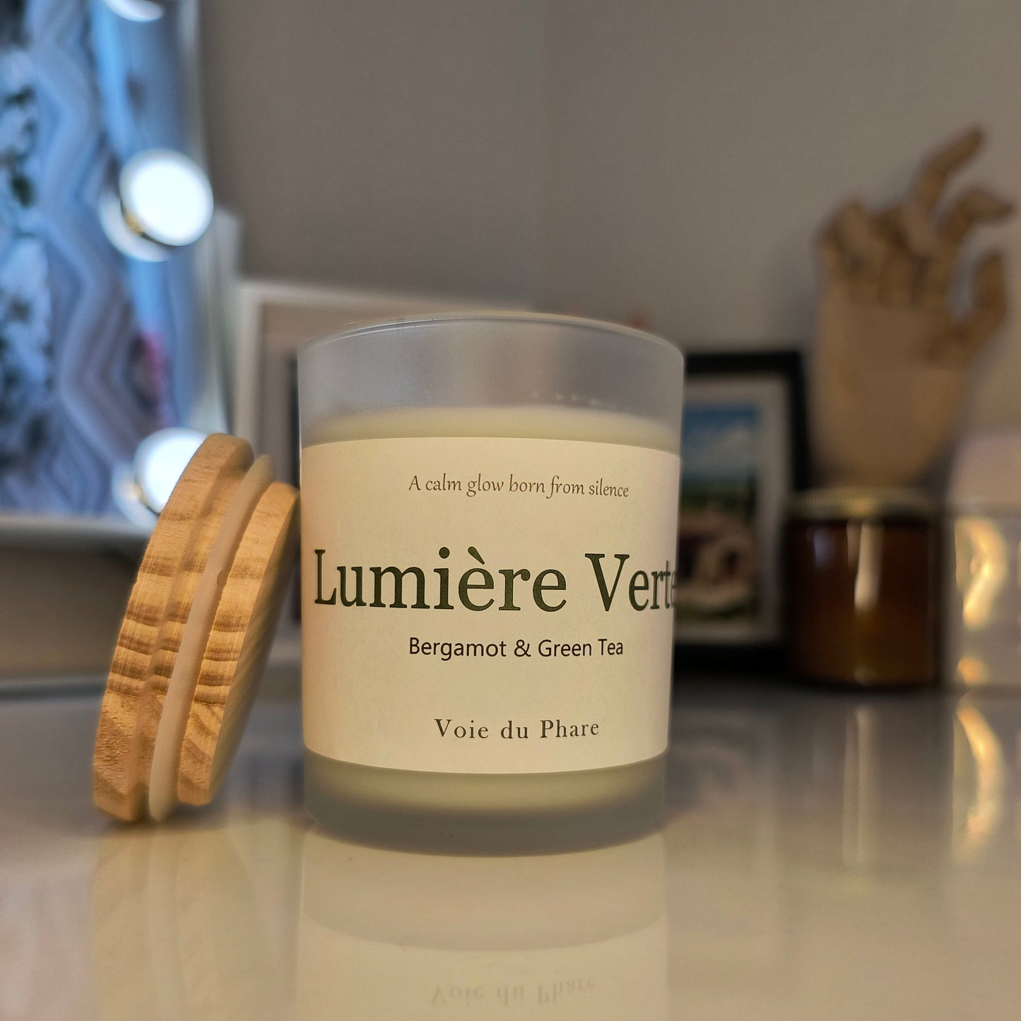 Candle with wooden lid labeled 'Lumiere Verte' on a reflective surface.