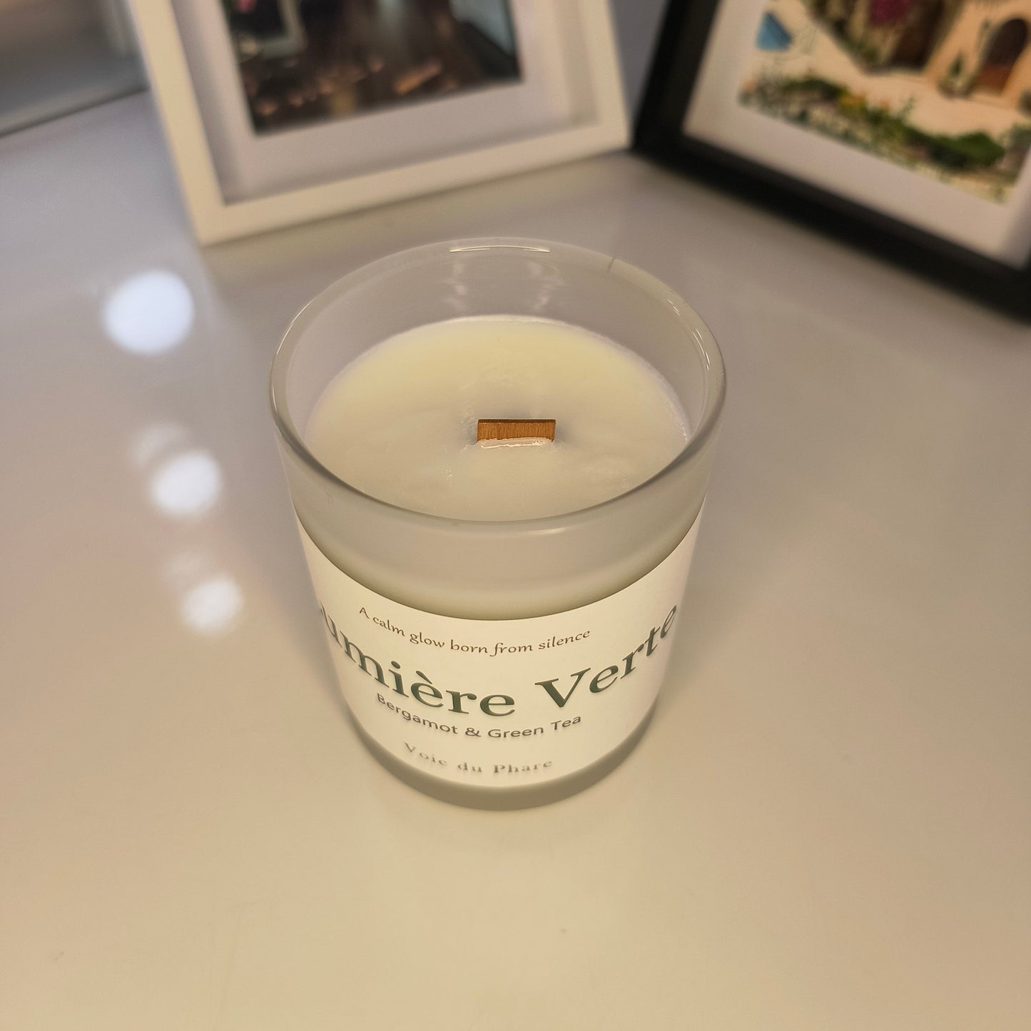 Jar of Lumiere Verte candle on a white surface with blurred background