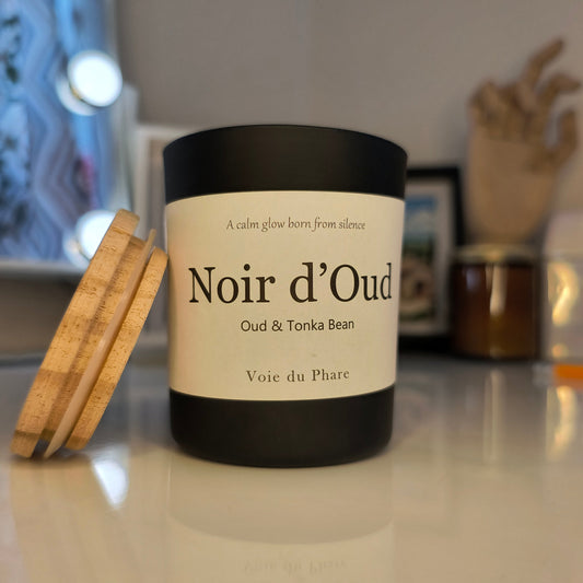 Candle labeled 'Noir d'Oud' with wooden wick on a blurred background
