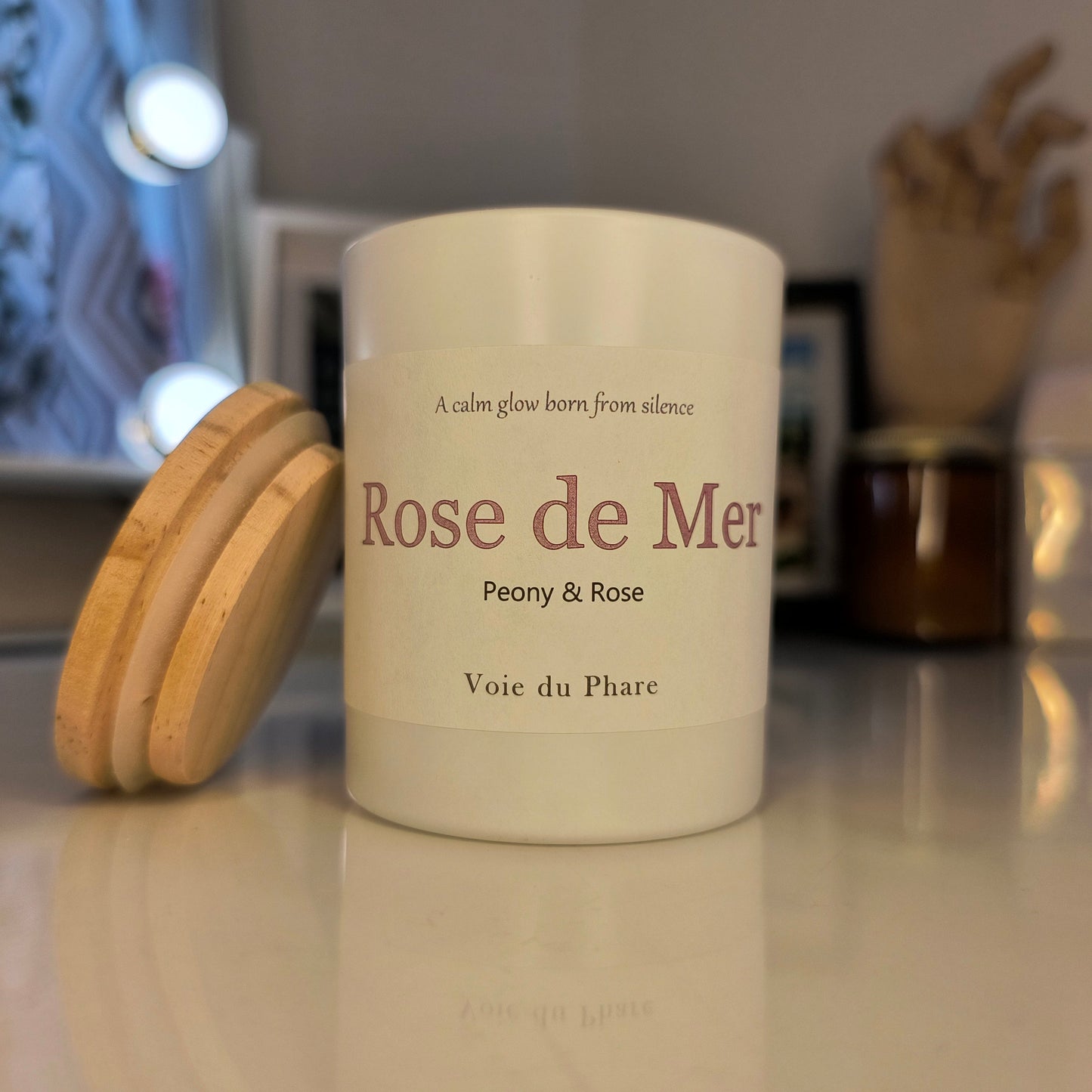 Candle labeled 'Rose de Mer' with wooden lid on a reflective surface