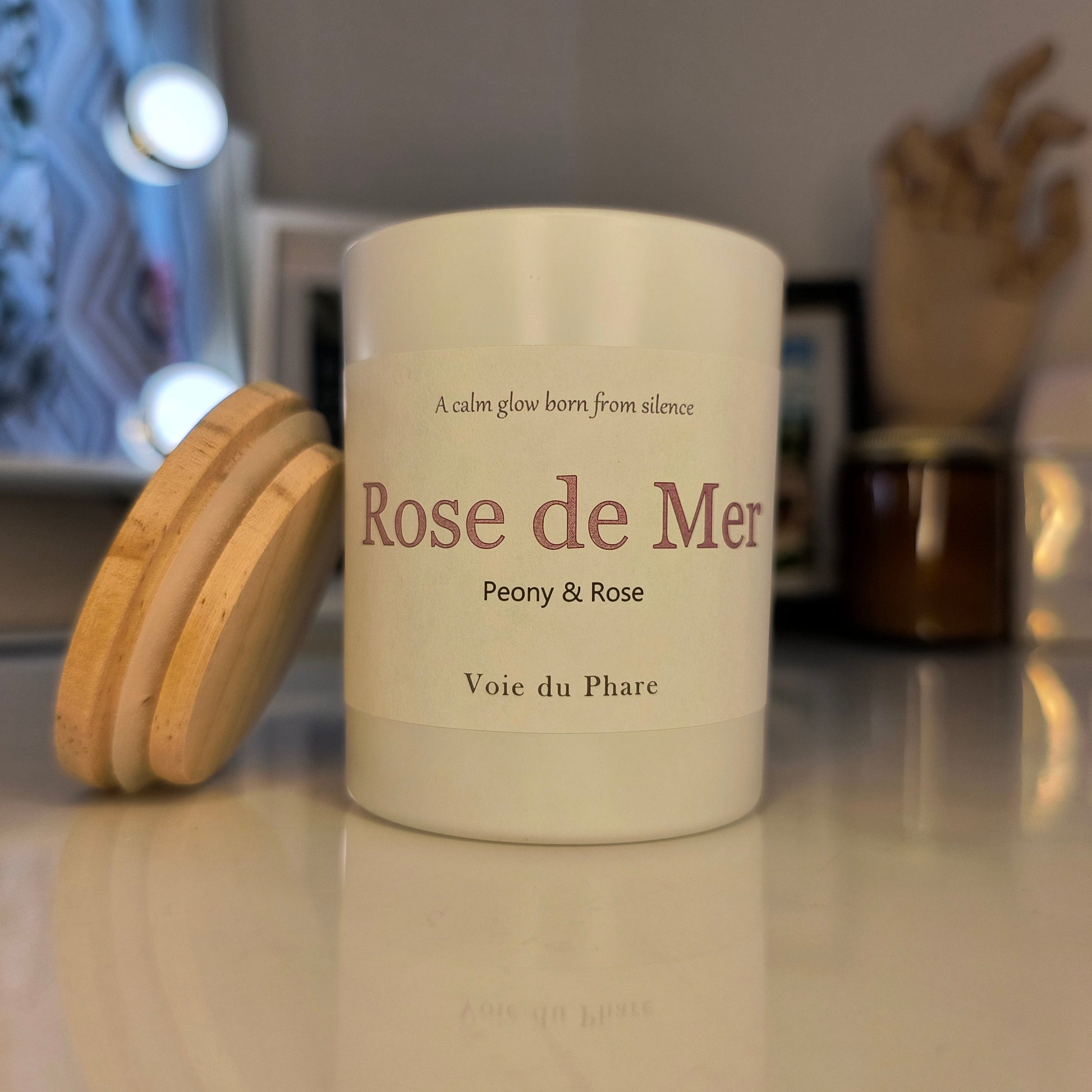 Candle labeled 'Rose de Mer' with wooden lid on a reflective surface