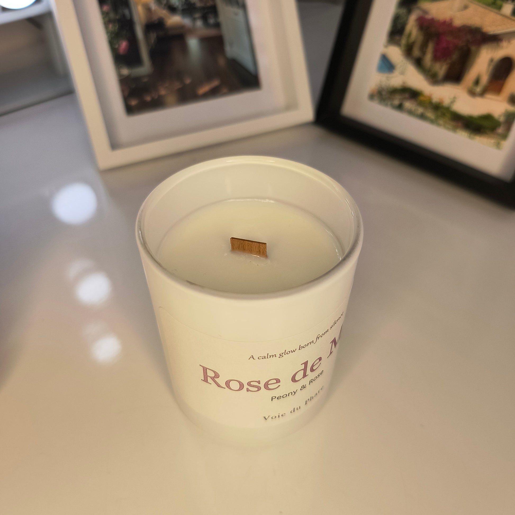 White candle in a decorative container with 'Rose de' text on a light background